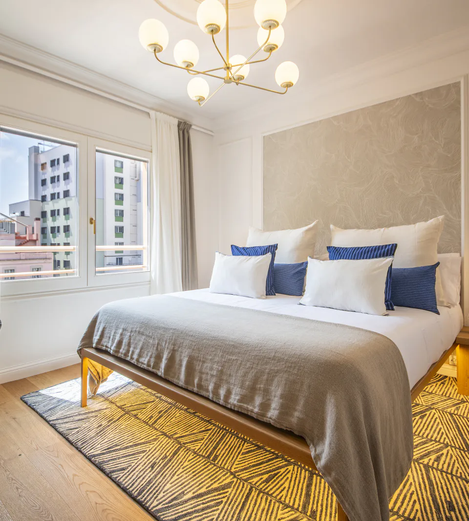 Suite Alba bedroom with city-facing windows and a sculptural chandelier