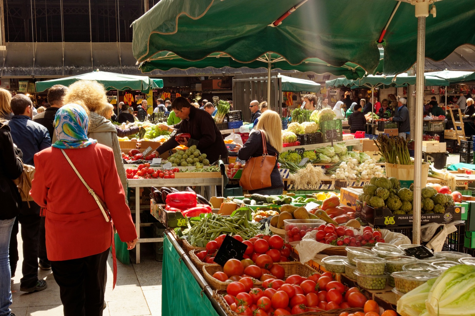 Shoppers passing colourful produce stalls inside La Boqueria market in Barcelona